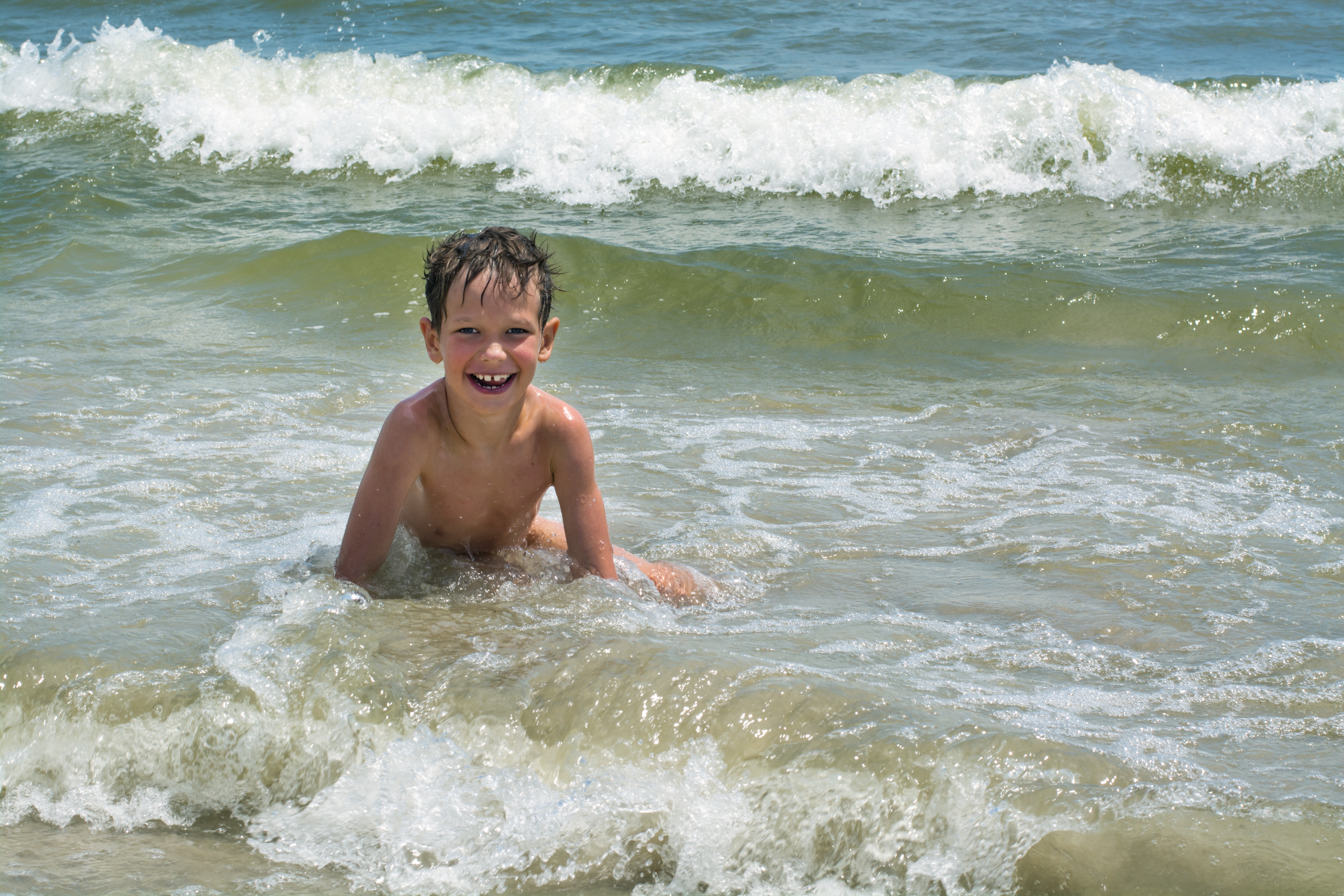 Cute happy baby boy bathes in the sea with waves, vacations © Adobe Stock